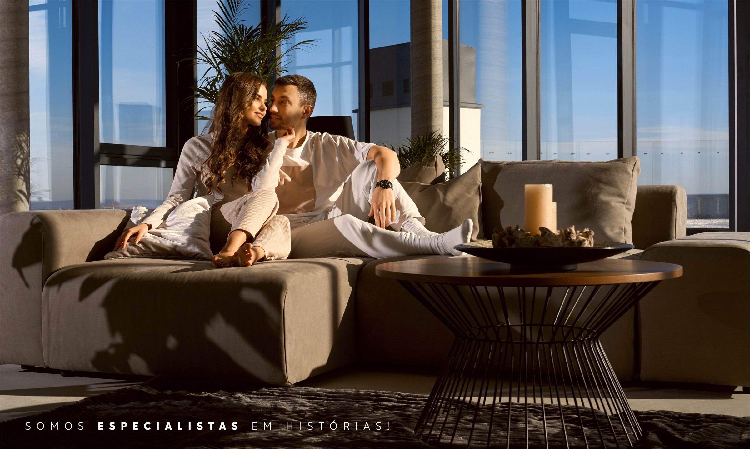 Casal no sofá de um apartamento de alto padrão com vista, e a frase Somos especialistas em histórias